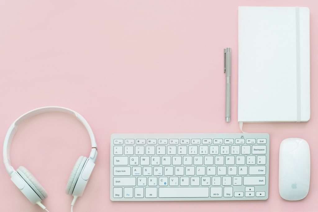 A white keyboard, mouse and headphones on a pink background.