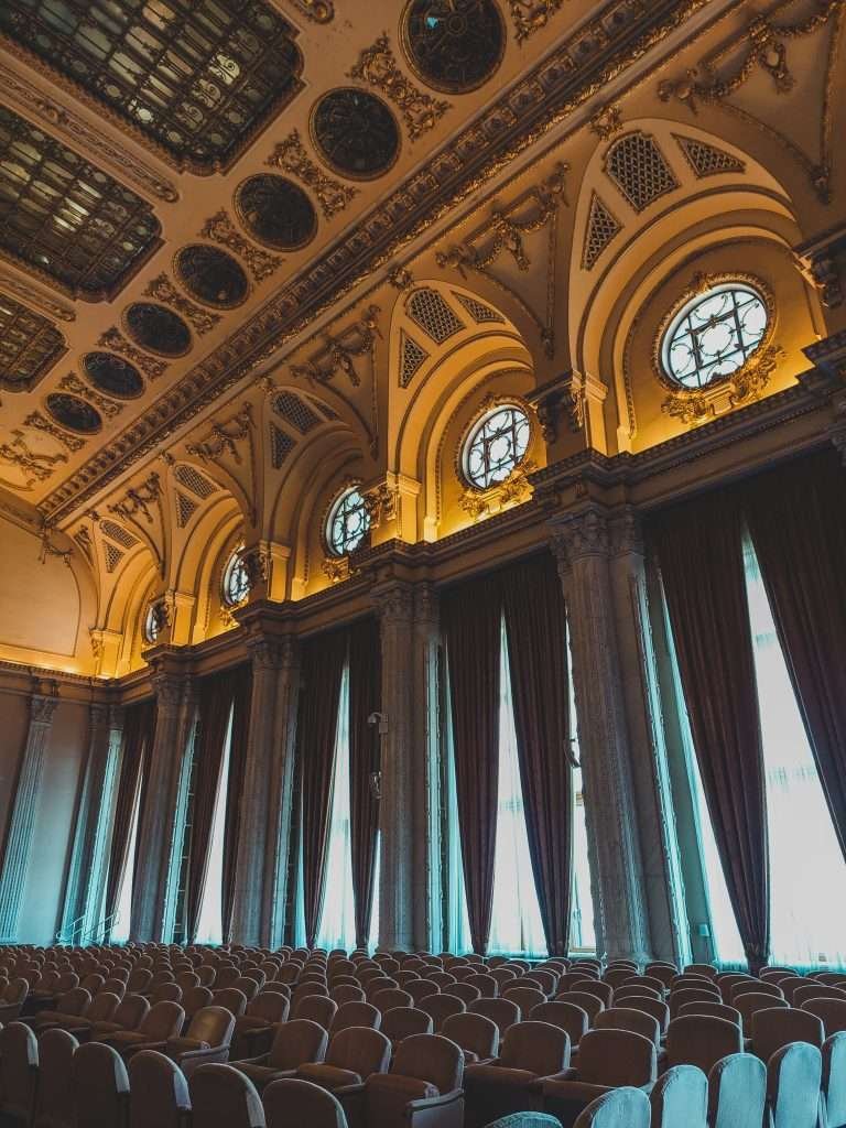 An empty auditorium with rows of chairs and windows.
