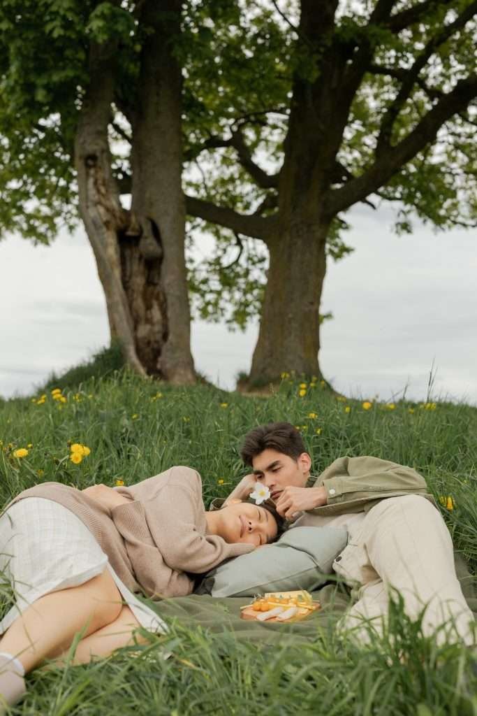 A man and woman laying on a blanket in a grassy field.